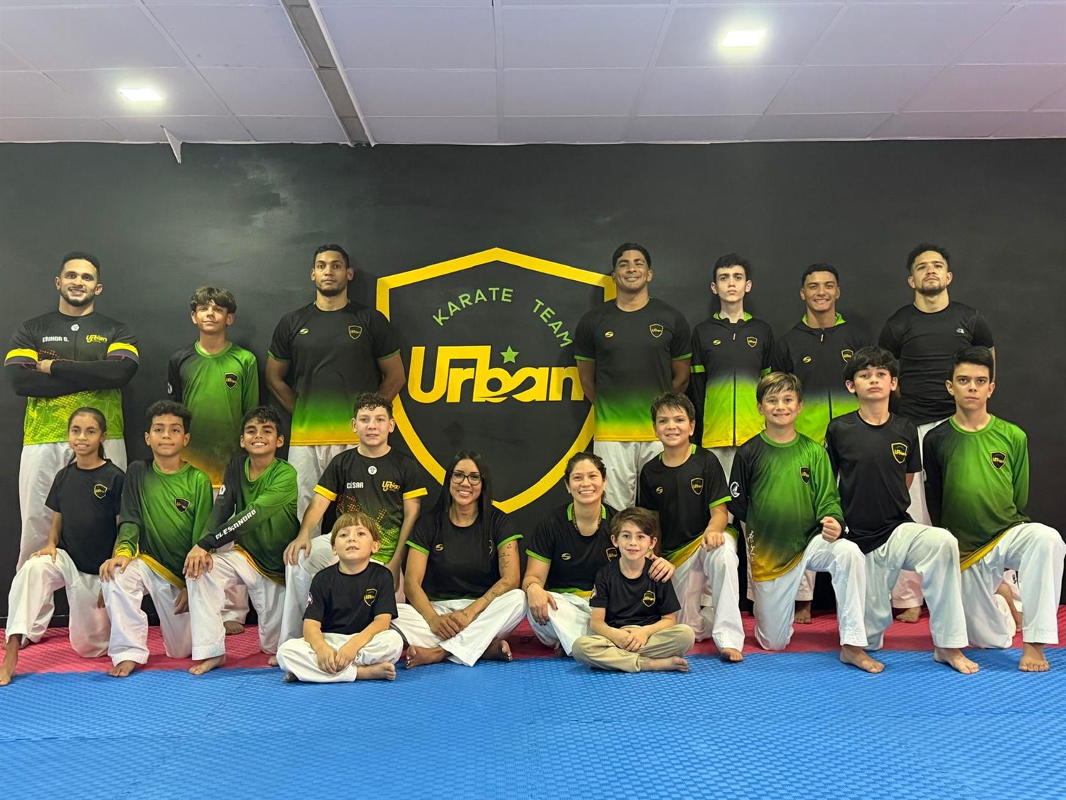 Niños y adultos de Urban Karate Team frente al escudo del club en el dojo de Venezuela
